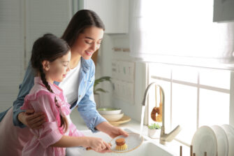 Mother and daughter washing dishes together in kitchen